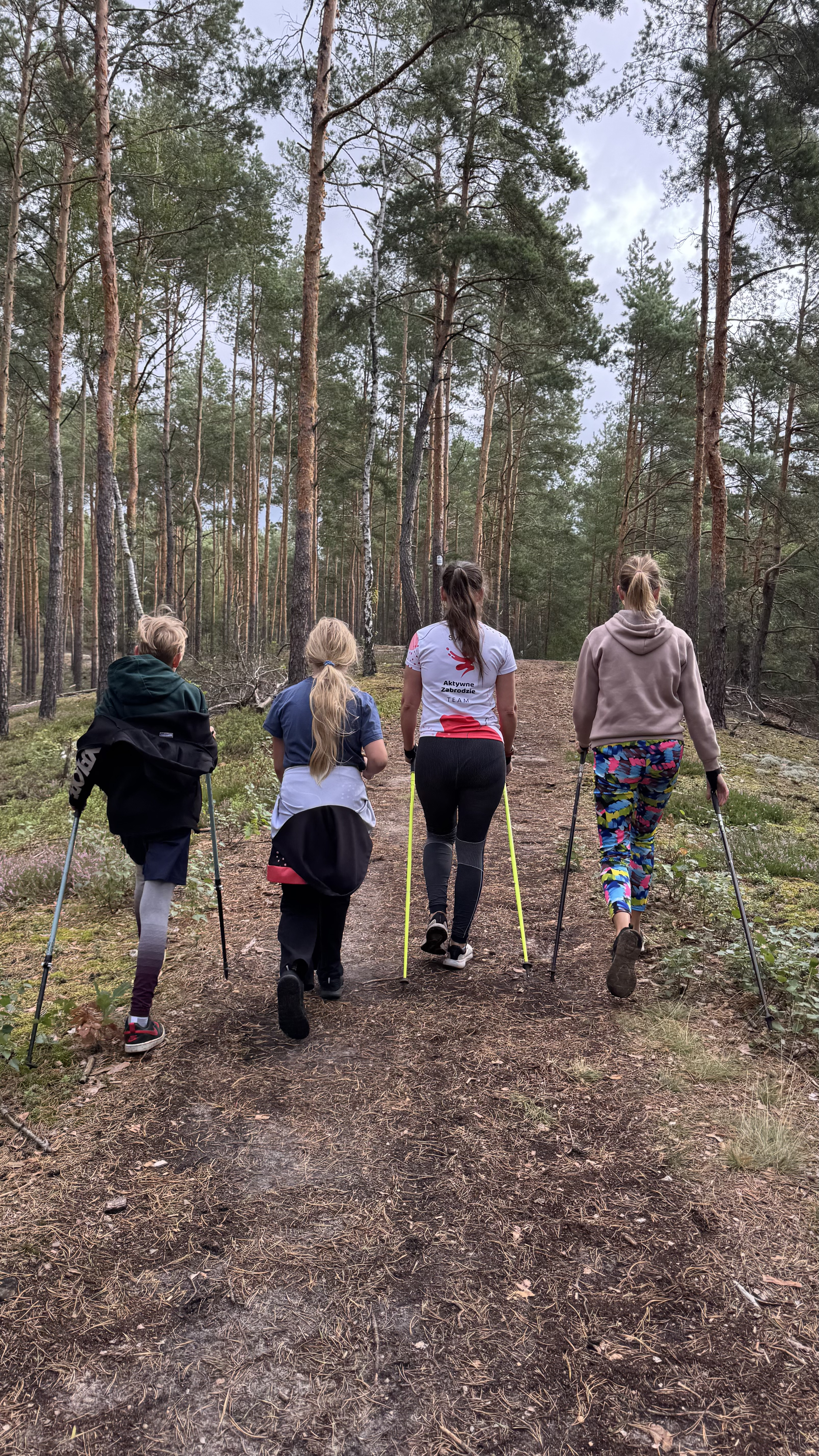 Uczestnicy treningu Nordic Walking idący przez las w Mostówce
